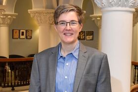 photo of smiling woman in glasses button down blue shirt and gray jacket