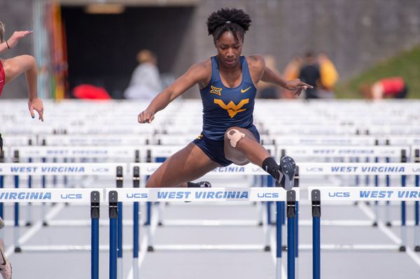  A female athlete that's part of the WVU track team is jumping hurdles during a race. 