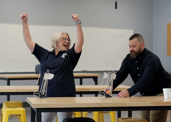 Two people standing in a classroom, one with their arms raised in celebration