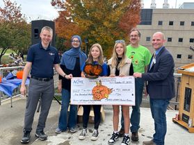The winning team for the 2023 WVU Pumpkin Drop holds a large check alongside three WVU faculty members.