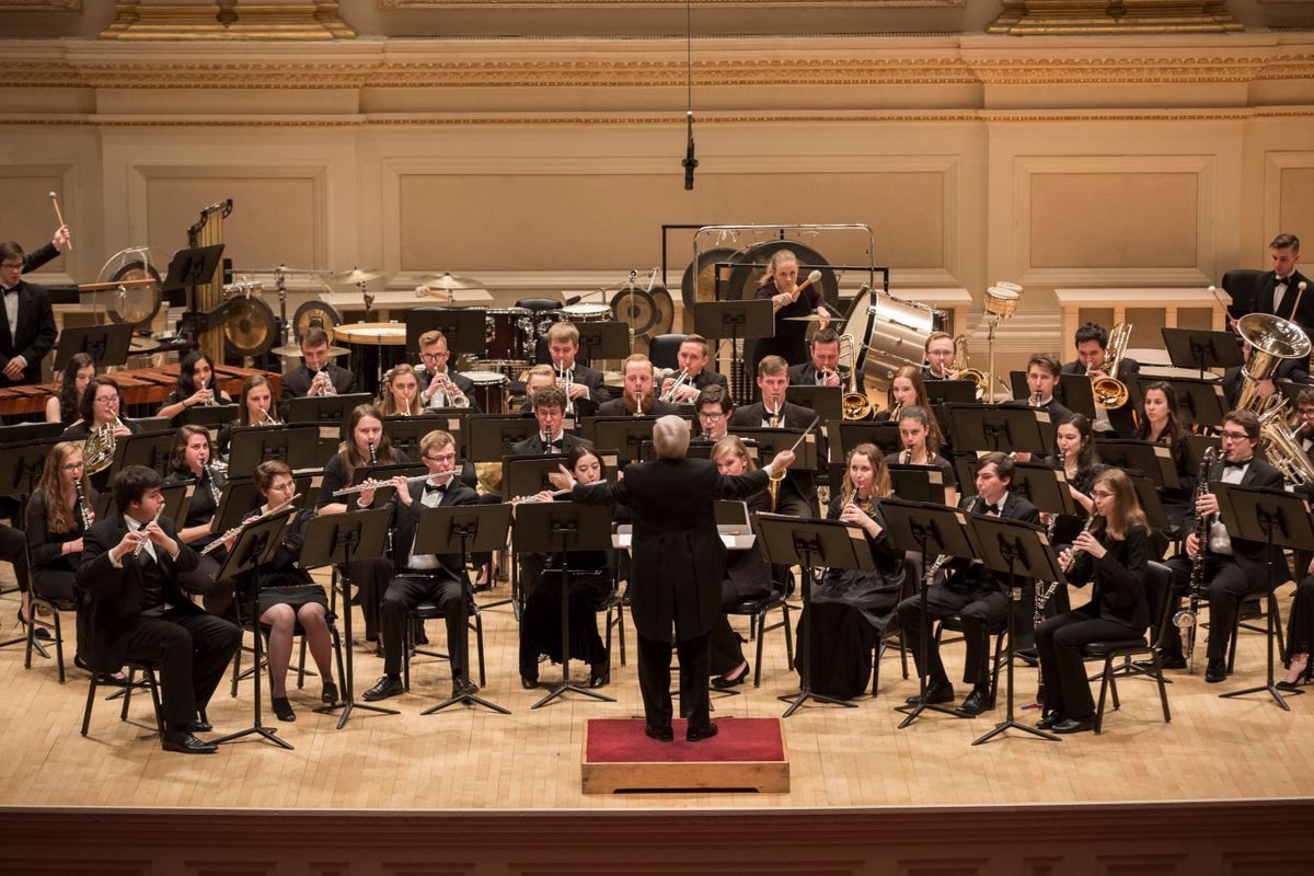 large group of musicians with instruments are seated on a stage with a conductor