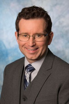 head shot of smiling white man is glasses and suit