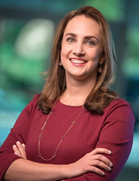 Headshot of WVU faculty member Laurel Cook. She is standing with her arms crossed in front of her wearing a red sweater. She has medium length brown hair and is wearing a long, gold necklace. 