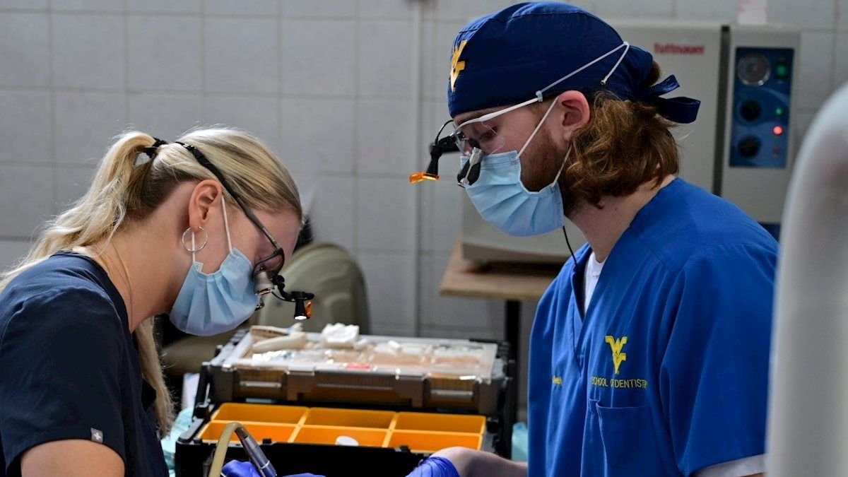 Photograph of two WVU School of Dentistry students working on a patient in a clinical setting. 