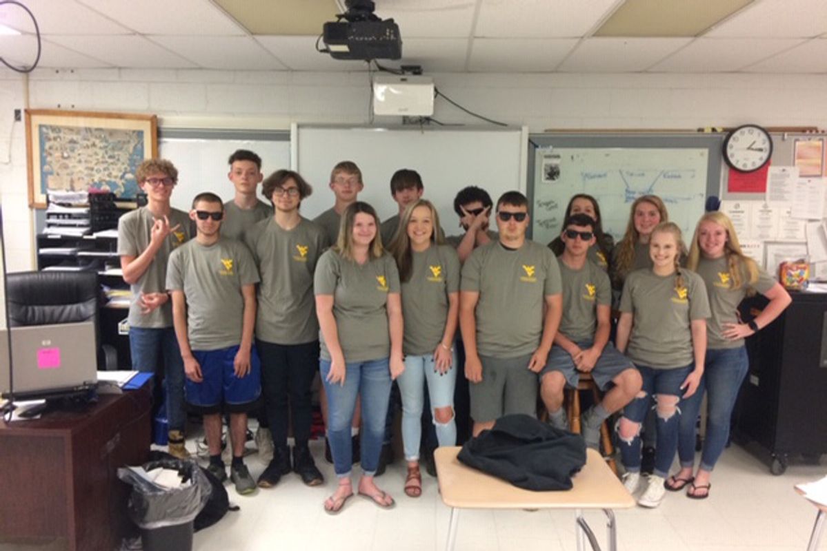 A group of 15 students in matching grey WV t shirts posing in a classroom for a photo.