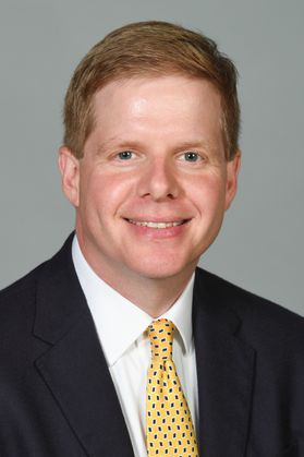 This is a portrait of Rob Alsop. He is smiling and wearing a dark suit jacket and gold tie.