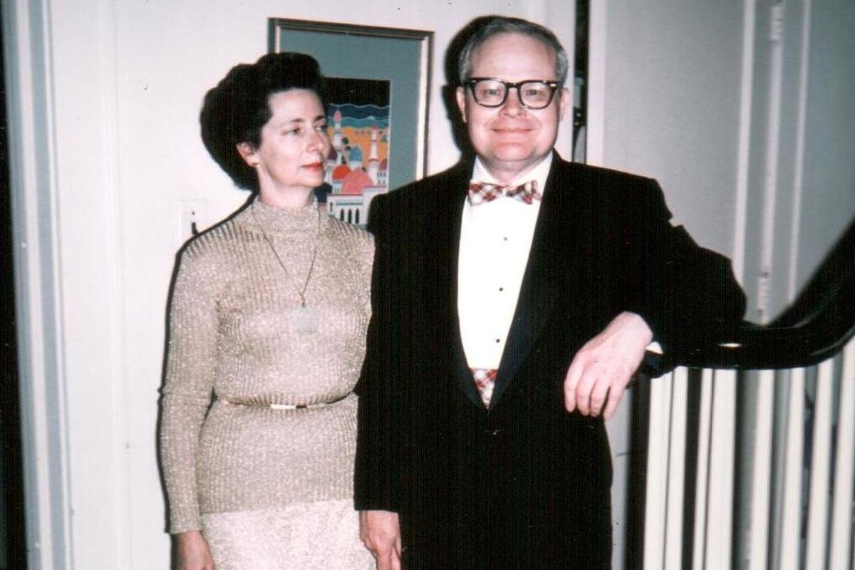 Woman wearing beige sweater with gold belt and a man wearing a black suit and white button-up shirt with bow tie