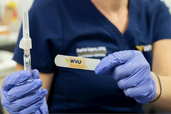 nurse in WVU Medicine scrubs holding up syringe and bandage