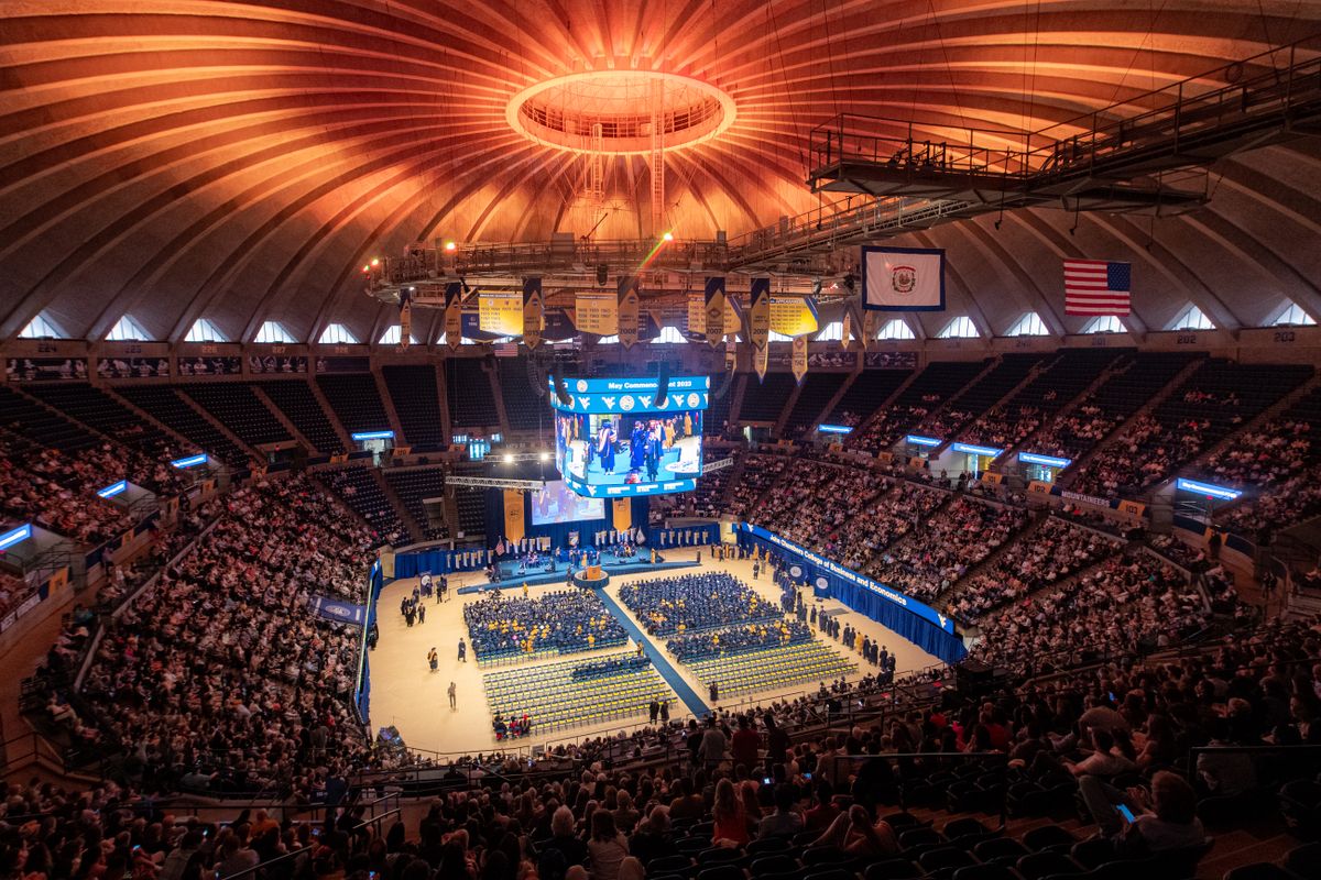 A picture of the WVU Coliseum during Commencement ceremonies in May 2023. Seats are filled with family members and well wishers, and chairs situated on the court are filled with graduates filing in the building. 