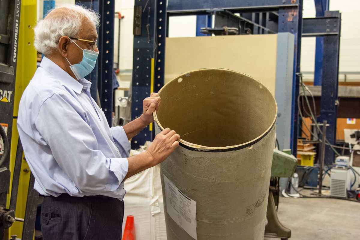older Indian man holding trash can with mask on