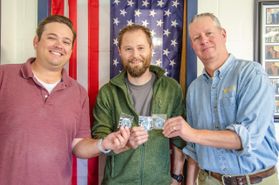 three men stand in front of an American flag holding buttons