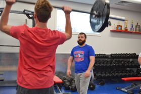 A man in a blue t-shirt watches a weightlifter
