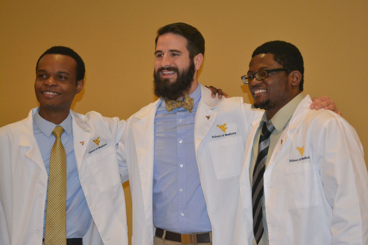 Three male students stand together after they receive their white coats