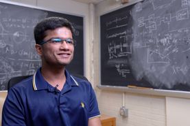 mans with glasses in front of chalkboards