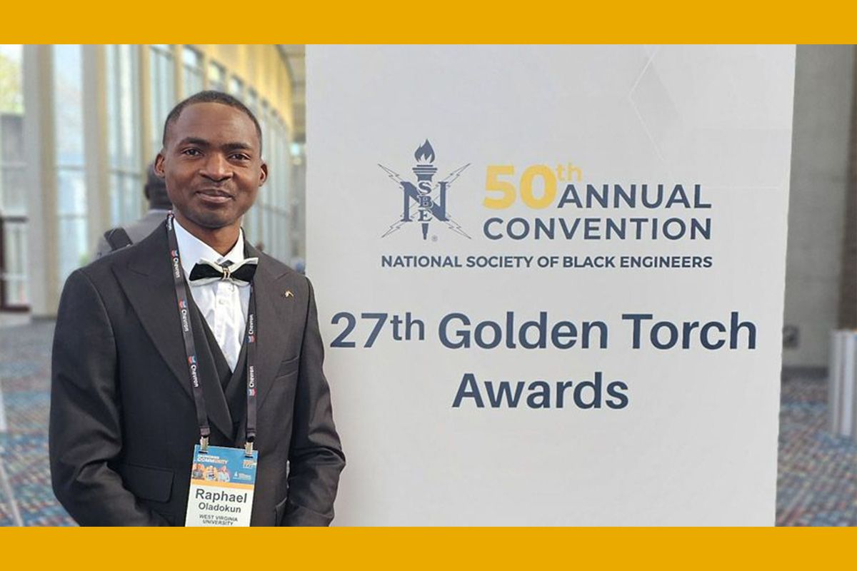 WVU student posing in front of a sign that says 27th Golden Torch Awards while wearing a dark suit and vest over a white shirt with a dark bowtie.