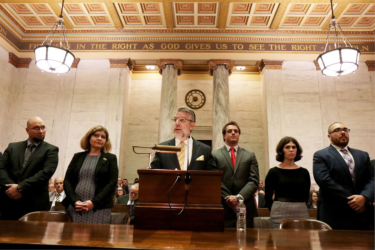 People are lined up behind a man at a podium