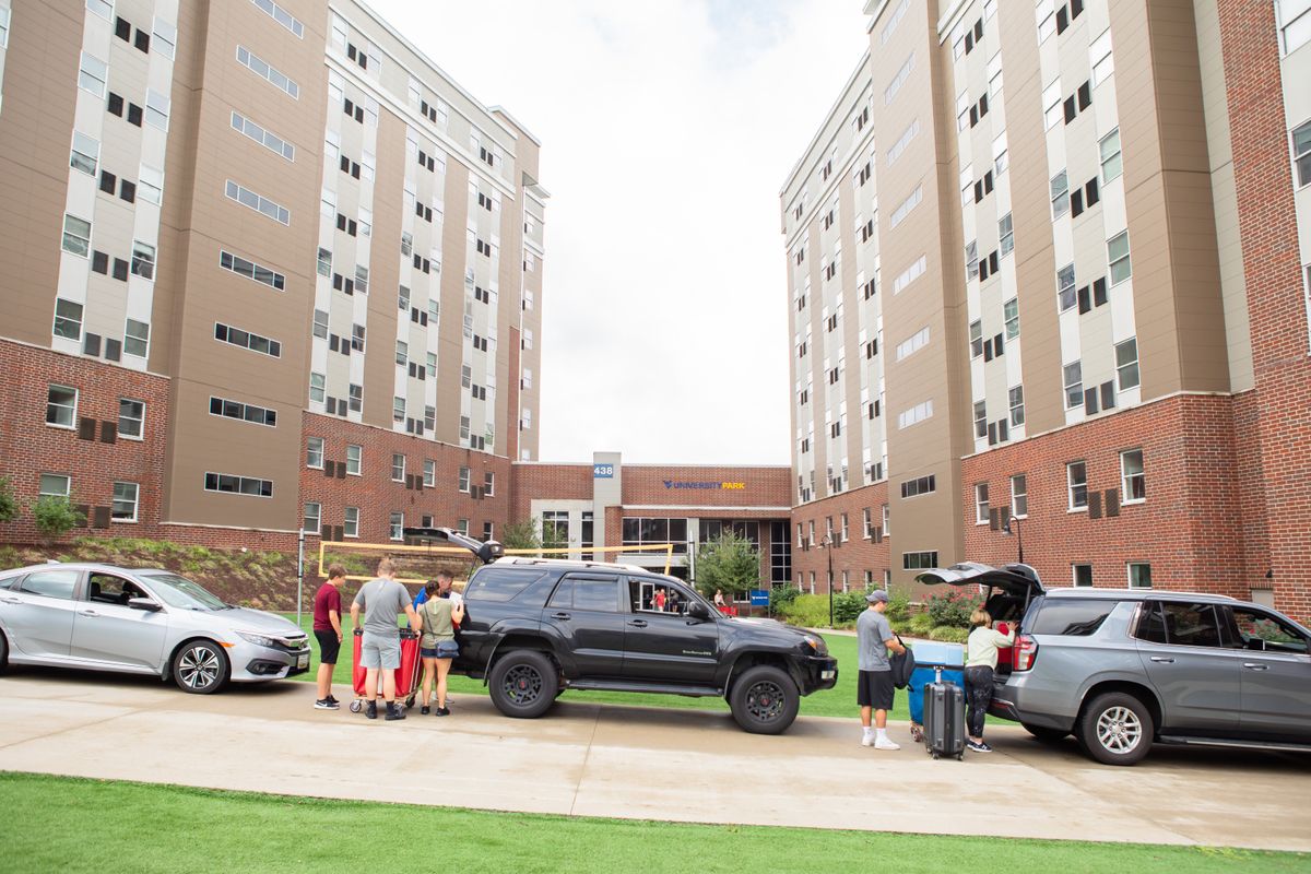 Vehicles parked outside of university dorms with people taking out bags and luggage 