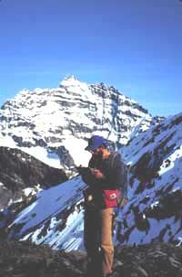Man with a clipboard in front of snow-covered high peaks