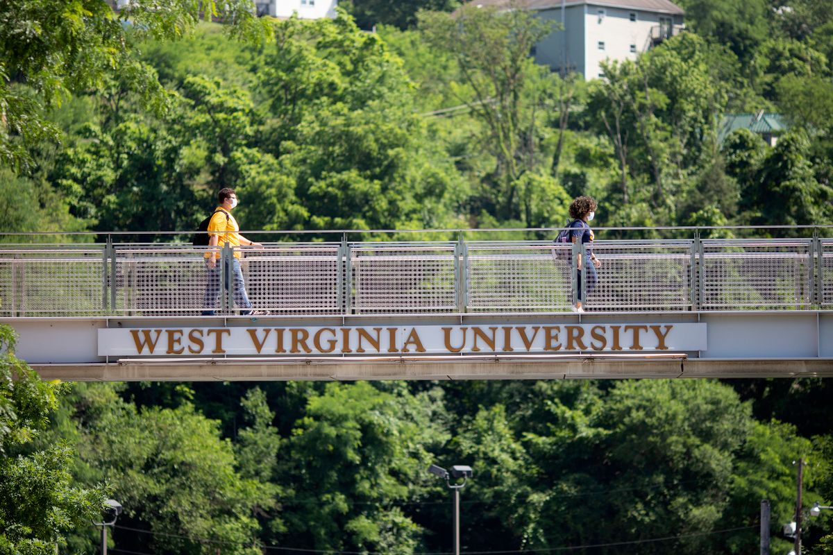 two people walk across West Virginia University bridge facing same direction, several feet apart