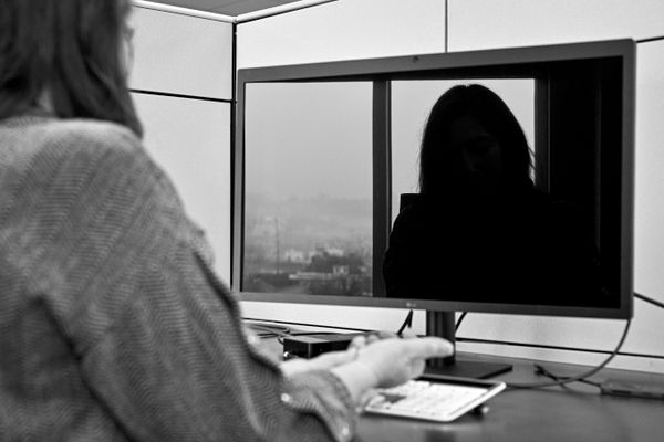 A black and white photograph showing a person sitting in front of a computer screen and their reflection is on the blank screen.