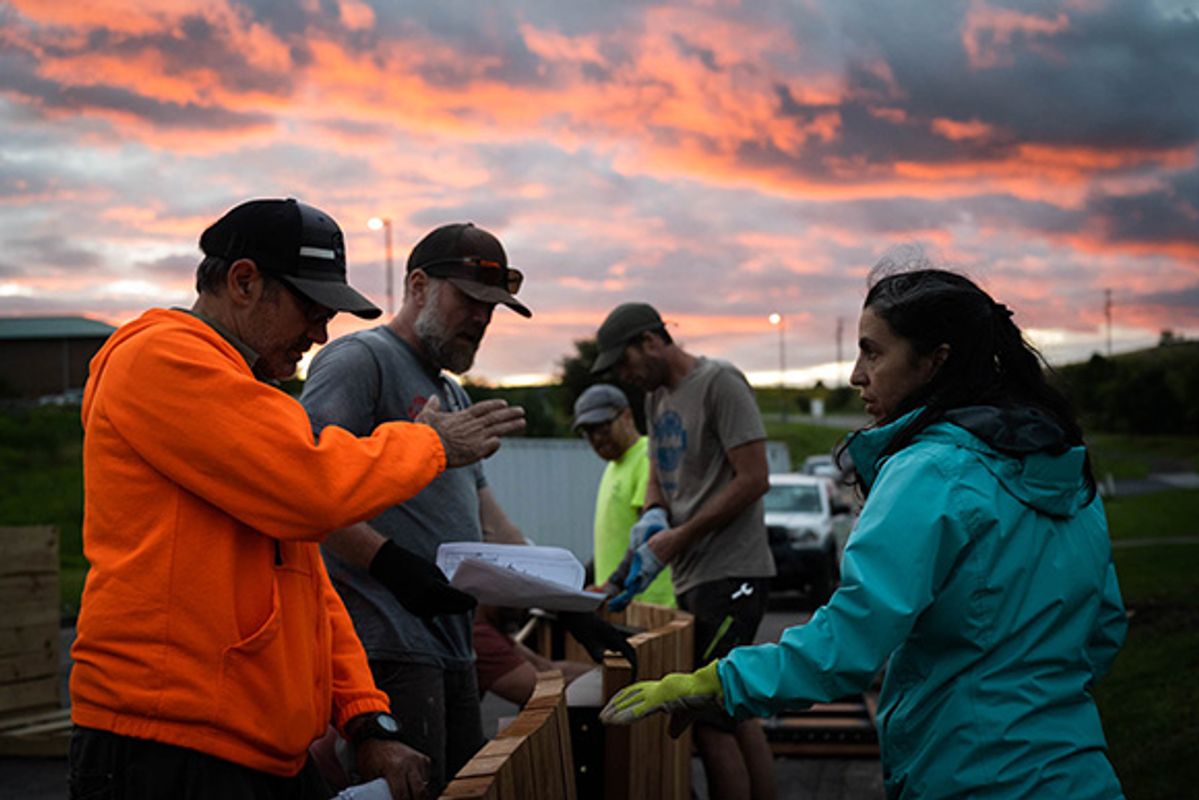 Image of volunteers working together to build a trail in Morgantown, West Virginia. There are five volunteers in the picture four men and one woman. There is a dazzling sunrise in the sky above them. 