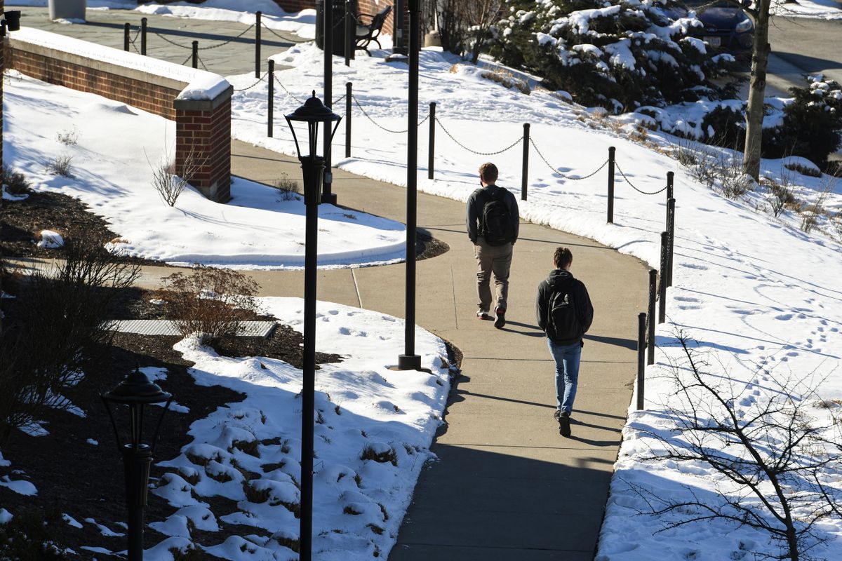 students walk on sidewalk amid snow covered hills