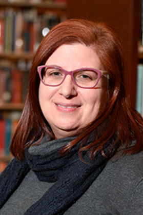 said Lori Hostuttler, WVRHC Interim Director, is pictured here wearing glasses, a turtleneck sweater, a black scarf, and shoulder-length red hair. 