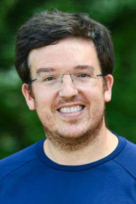 photo of smiling man in glasses and royal blue shirt