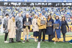 The Most Loyal Mountaineers stand on Mountaineer Field holding plaques alongside WVU President Gordon Gee.