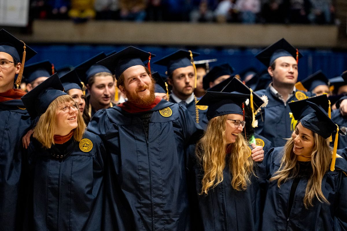 A group of WVU graduates dressed in their navy blue caps and gowns celebrates together during fall 2022 Commencement ceremonies. There numerous people in the photograph with three women and three men in sharp focus. 