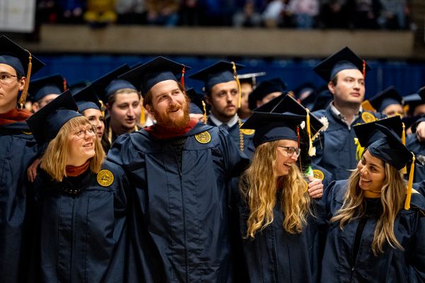 A group of WVU graduates dressed in their navy blue caps and gowns celebrates together during fall 2022 Commencement ceremonies. There numerous people in the photograph with three women and three men in sharp focus. 