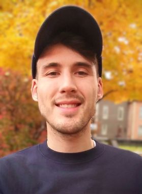 Headshot of WVU student Andrew Ross. He is pictured outside with a fall tree behind him. He is wearing a black shirt and a black baseball cap. 