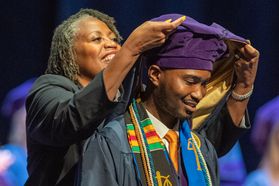 Black woman puts graduation hood on black man during ceremony