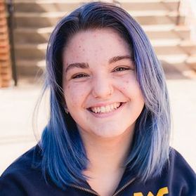 Headshot of WVU student Wren King. They are pictured outside wearing a navy blue WVU branded shirt. They have dyed blue hair.