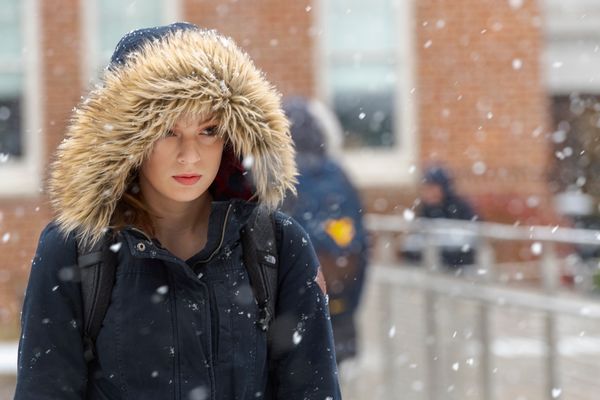 A girl in a coat with a fur hood walks in the snow