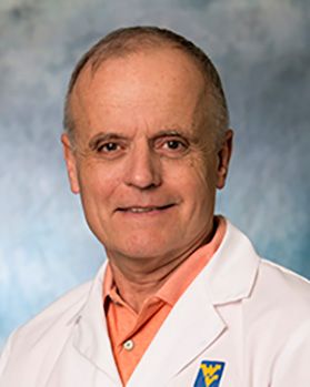 Headshot of WVU researcher Mark Polak. He is pictured against a mottled gray background and is wearing a peach collared shirt under his white lab coat. He has very short dark hair. 