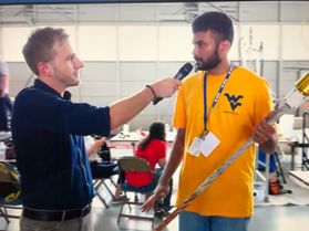 photo of man interviewing man in gold flying WV shirt