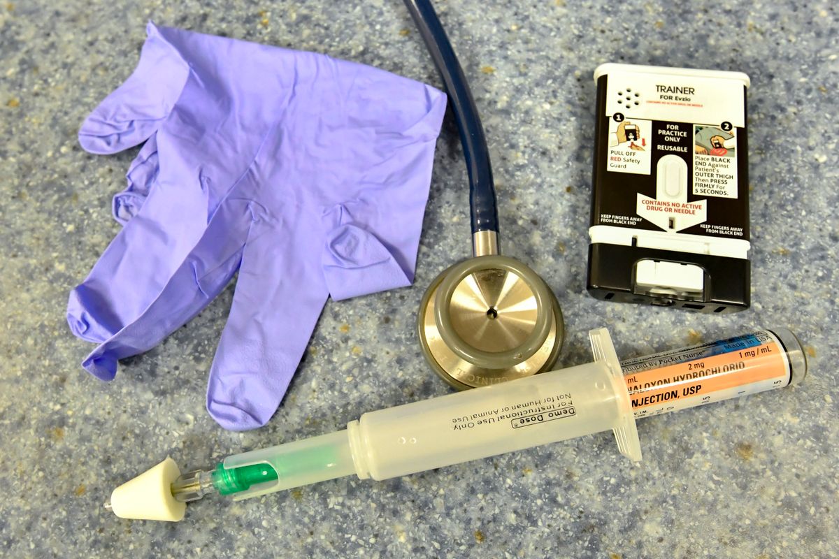 photo of a purple latex glove, syringe with cap over the needle, stethescope and small box that says trainer