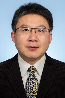 Man in a black suit, with patterned tie and glasses