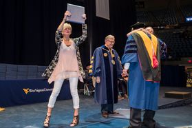 arrie Dworshak holds up the posthumous degree belonging to her late son Calvin as her daughter Avery hugs Dean Dan Robison. Calvin unexpectedly passed away last March and this would have been his commencement ceremony. He was recognized during the Davis C