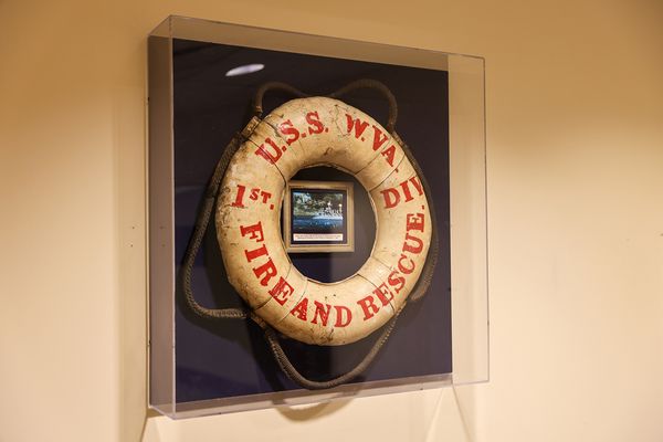 A white life preserver from the USS West Virginia is mounted in a clear frame on a wall. 