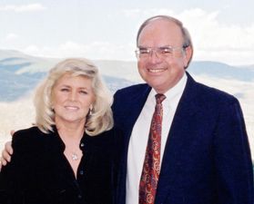 Photograph of Randy and Ken Kendrick, generous donors to WVU. Randy is wearing a black jacket and has shoulder length blond hair. Ken is wearing a blue jacket, a white dress and a red patterned tie. 
