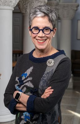 A portrait of Maryanne Reed who is standing with her arms crossed in a black and gray sweater.