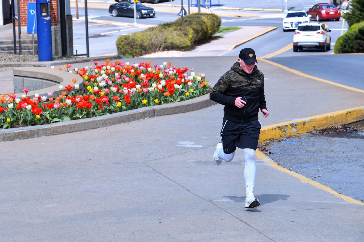 man in shorts, leggings, cap runs on an empty sidewalk