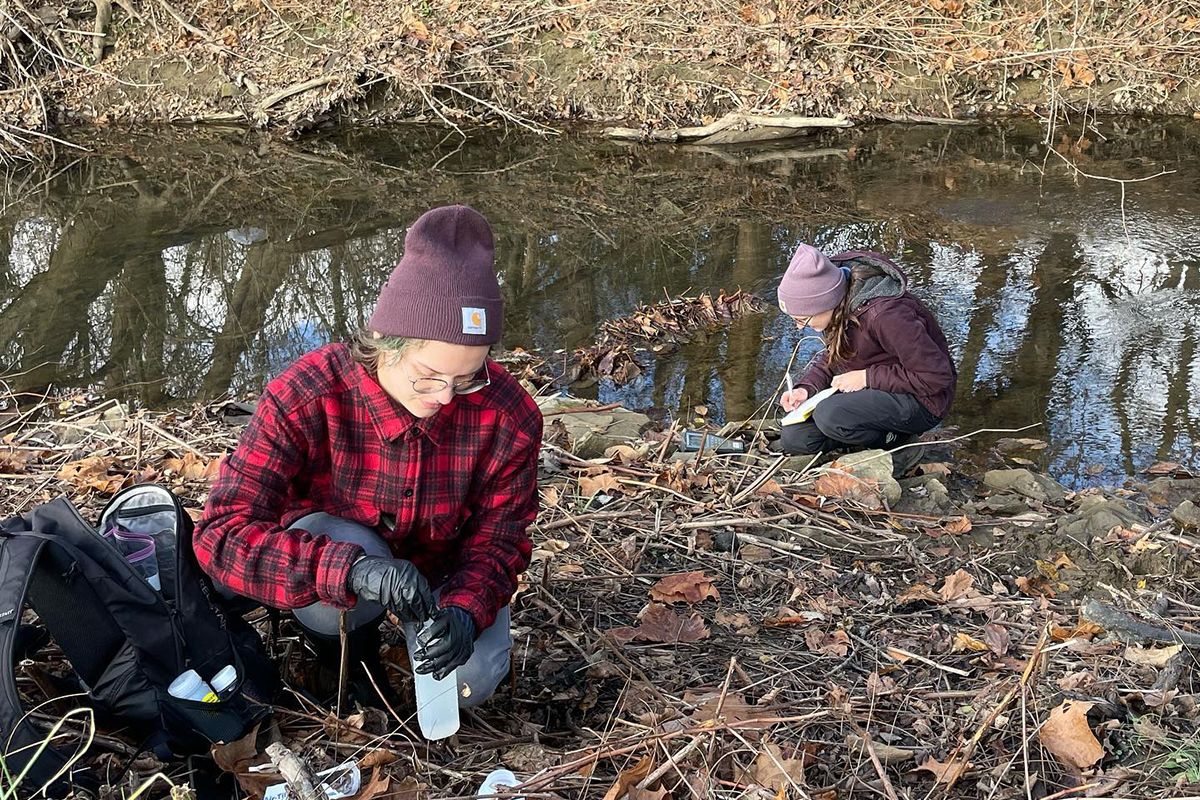Two WVU researchers, dressed in warm clothing, take water samples from a small creek