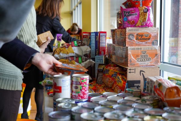 Image features canned goods and other non perishable food items on a table collected to help alleviate food insecurity in West Virginia. There are people in the image put only their hands as they place items on the table. 