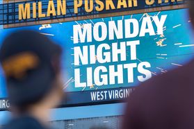 Two blurred heads look at the football field's sign that reads "Monday Night Lights"