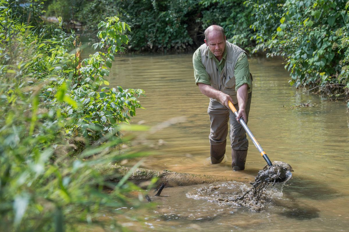 photo of man dredging a stream with a basket tool