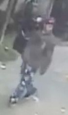 This is a fuzzy surveillance image showing a burglary suspect who is wearing ripped jeans, a dark jacket or shirt and red hat.