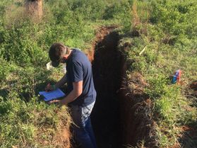 student takes soil samples in a hole